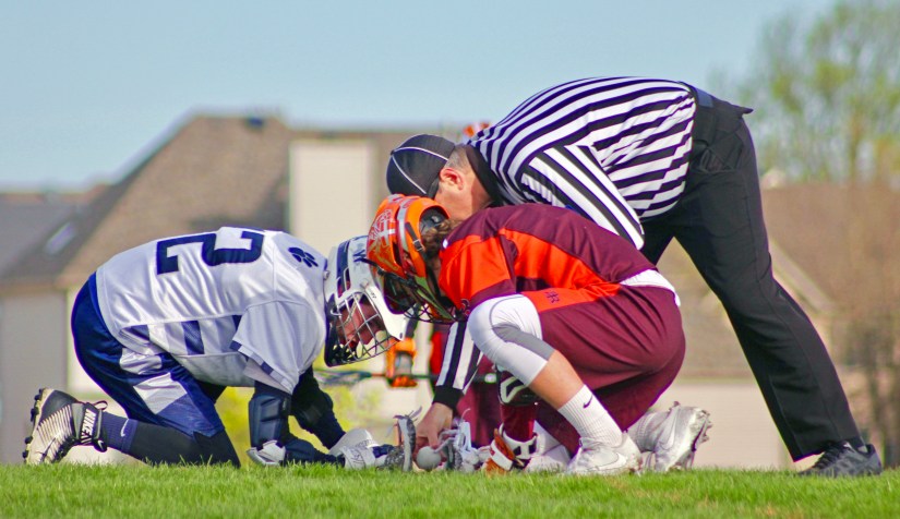 Referee_placing_ball_between_middies_for_a_lacrosse_faceoff.jpg